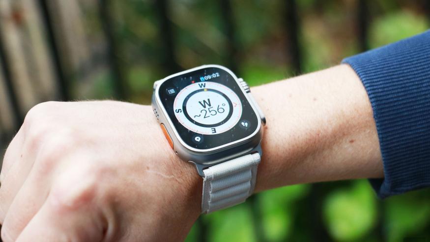 The Apple Watch Ultra on a wrist held in mid-air with a compass on its screen. The compass is showing the letter W with "~256 degrees" below it.